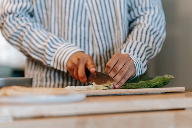 Person in striped shirt chopping lettuce on wooden cutting board in kitchen