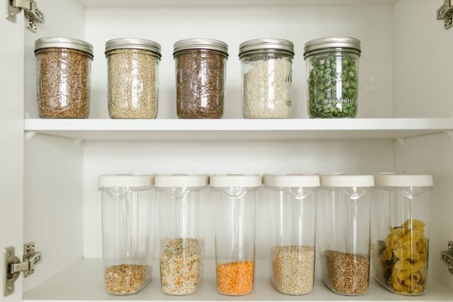 Organized pantry shelf with glass jars filled with grains, rice, green peas and pasta